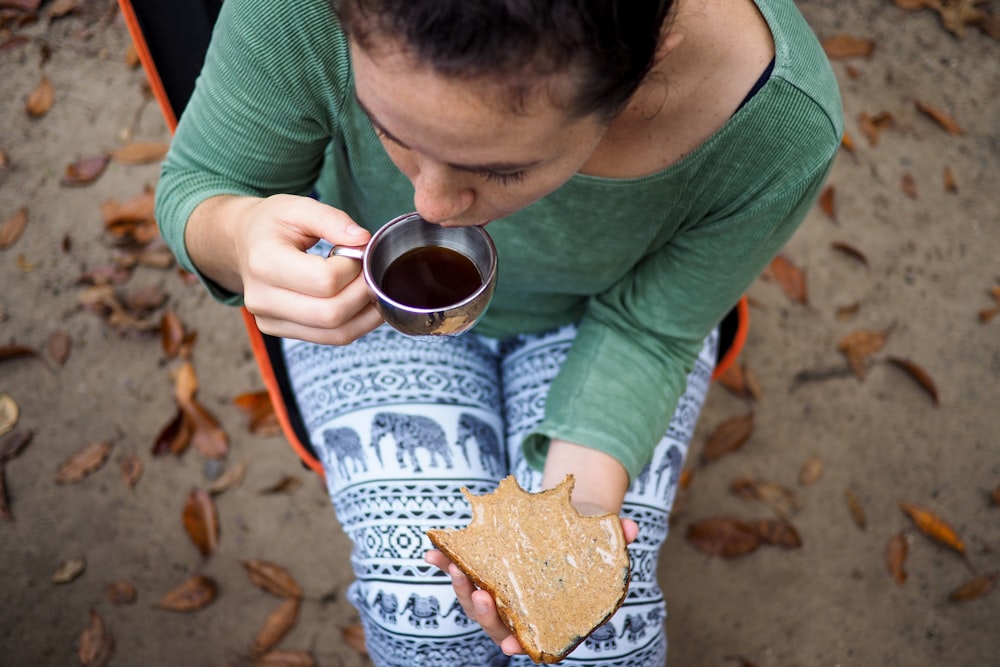 femme tenant une tasse en acier gris et un toast à l’extérieur pendant la journée