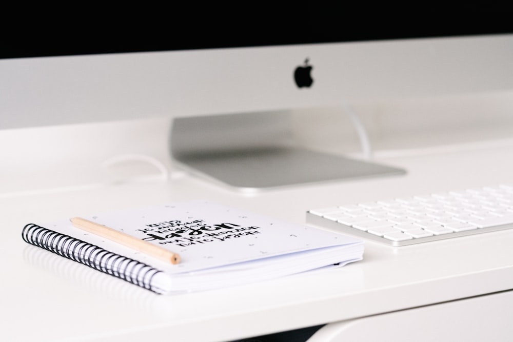 livro branco ao lado do iMac e teclado na mesa