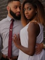 man embracing woman in front of gray wall