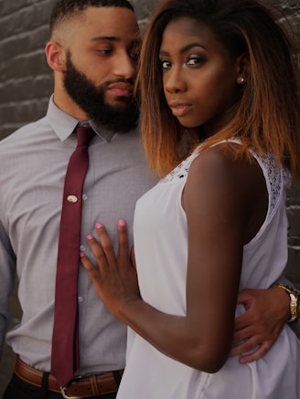 man embracing woman in front of gray wall