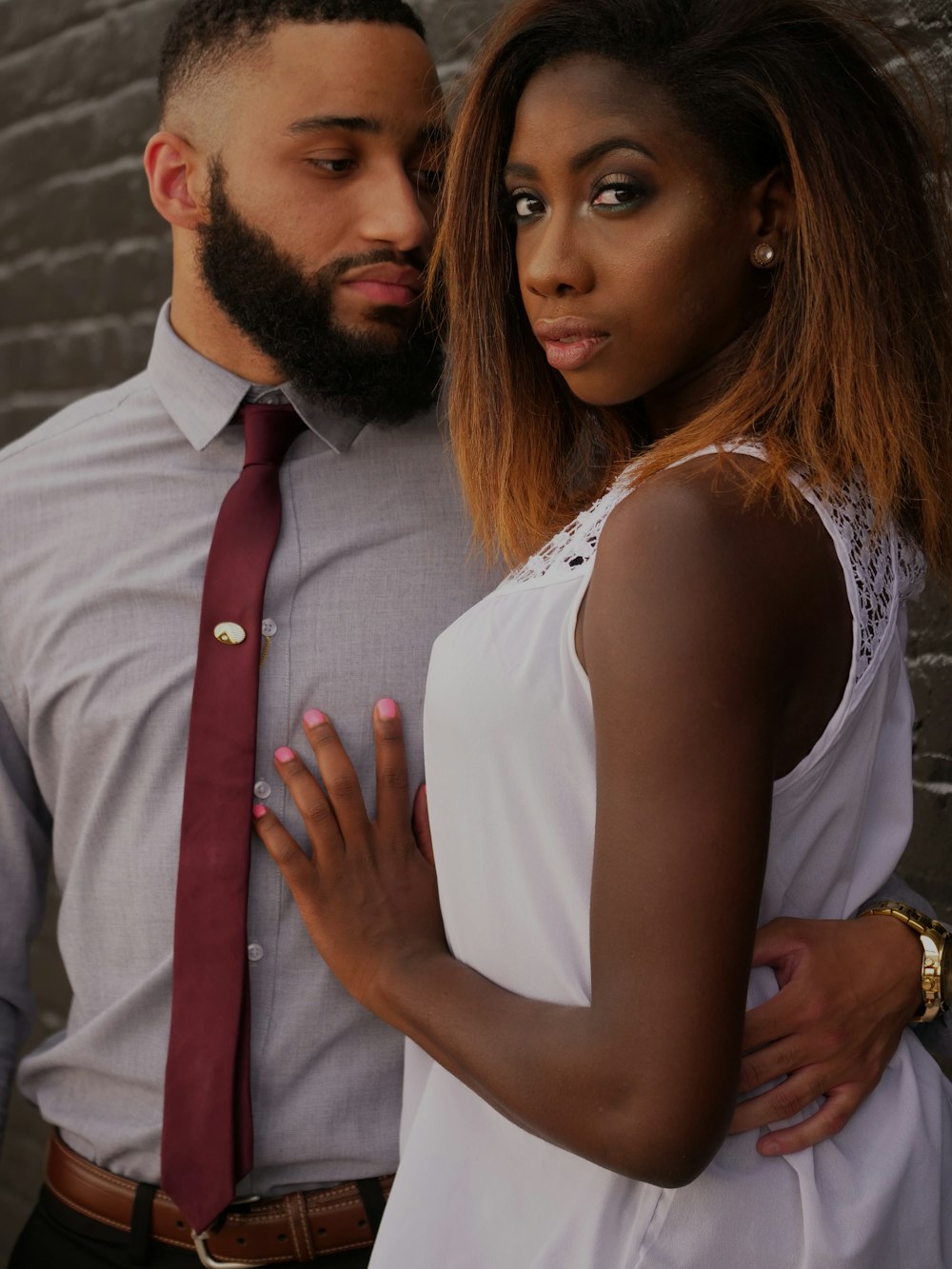 man embracing woman in front of gray wall