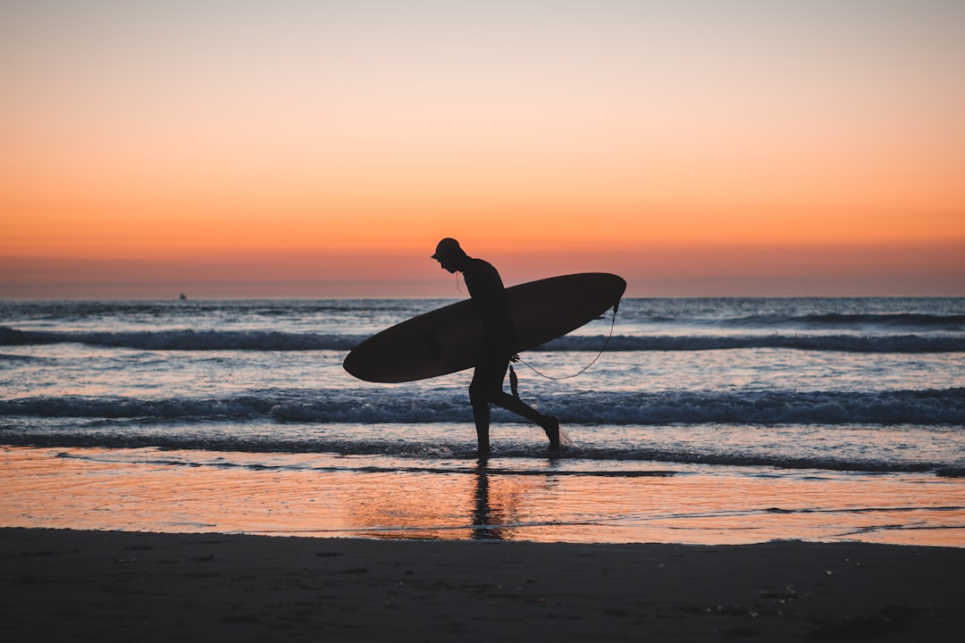 silhouette photo of person holding surfboard near shore, Sunset Surfer
