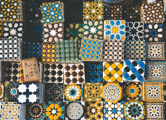 A collection of decorative tiles featuring intricate geometric and floral patterns in a variety of colors such as blue, yellow, black, and white. The tiles are arranged closely together, showcasing a rich tapestry of cultural designs and artistic craftsmanship.