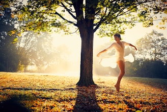 woman spreading arms beside tree during daytime