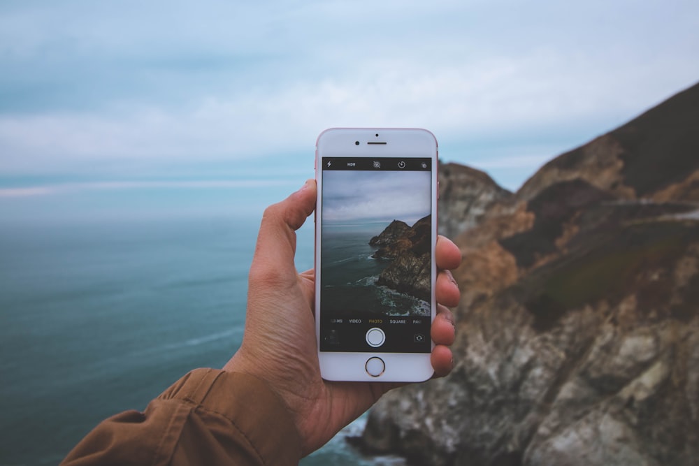 person taking photo of a ridge by sea