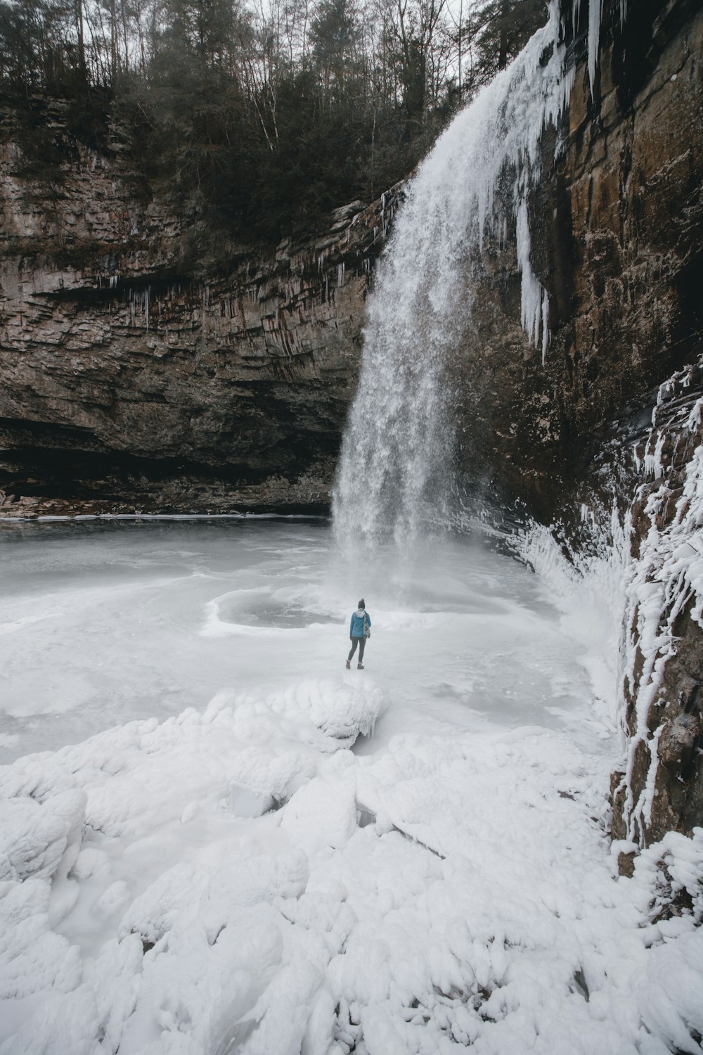person standing on frozen waterfall outdoor during daytime