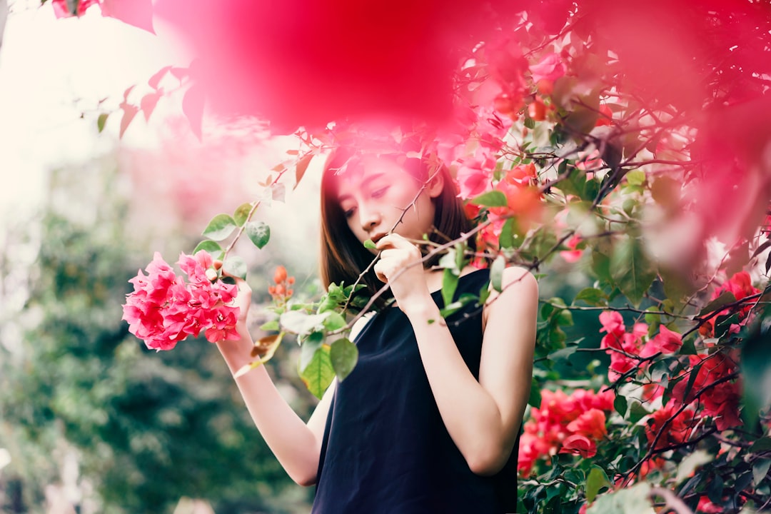 woman in black sleeveless top holding branch of plants with red flowers