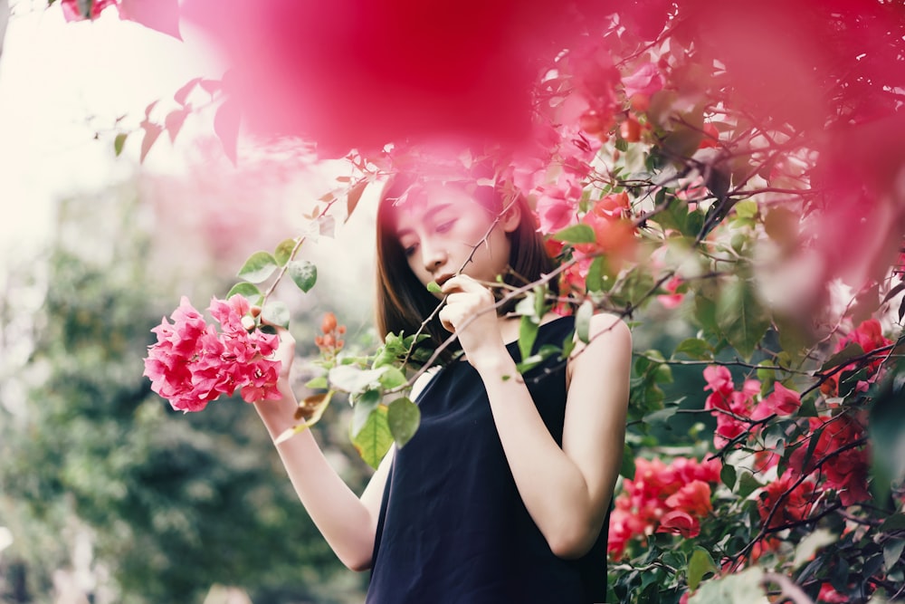 Femme en haut noir sans manches tenant une branche de plantes à fleurs rouges