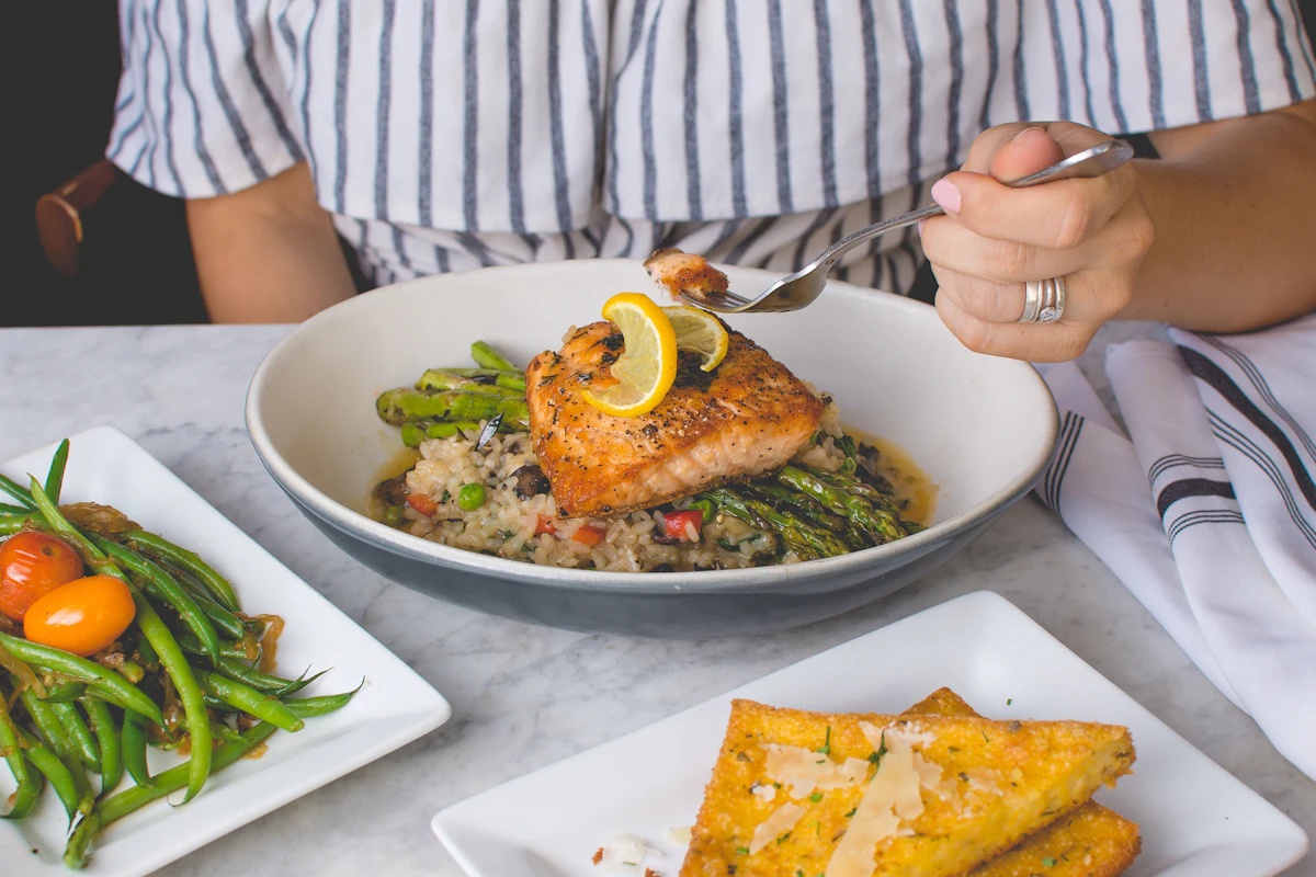 A plate of salmon with greens and lemon on a table set for lunch