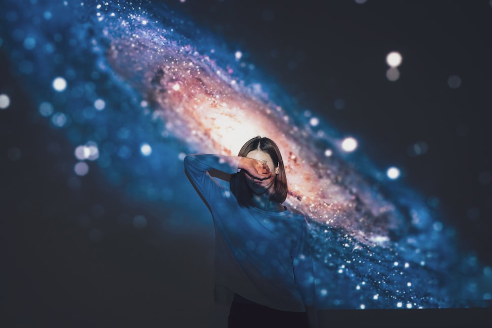 mulher cobrindo seu rosto usando a mão direita com fundo da galáxia