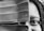 A close-up black and white photo of a person's face partially obscured by a large leaf, with the focus on one visible eye and braided hair.