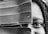A close-up black and white photo of a person's face partially obscured by a large leaf, with the focus on one visible eye and braided hair.