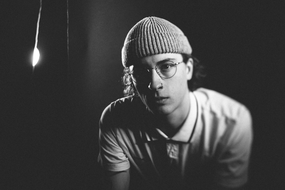 grayscale photography of man in knit cap and eyeglasses near wall