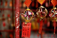Colorful decorative ornaments with intricate designs hang from a rod, featuring golden frames and paper elements with floral patterns. Red tags with Chinese characters are attached, adding a cultural and festive touch.