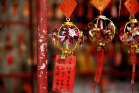 Colorful decorative ornaments with intricate designs hang from a rod, featuring golden frames and paper elements with floral patterns. Red tags with Chinese characters are attached, adding a cultural and festive touch.