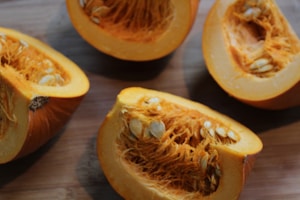Several pieces of a pumpkin cut into halves display the vibrant orange flesh and numerous seeds. The image captures the texture of the stringy interior and the smooth outer rind.