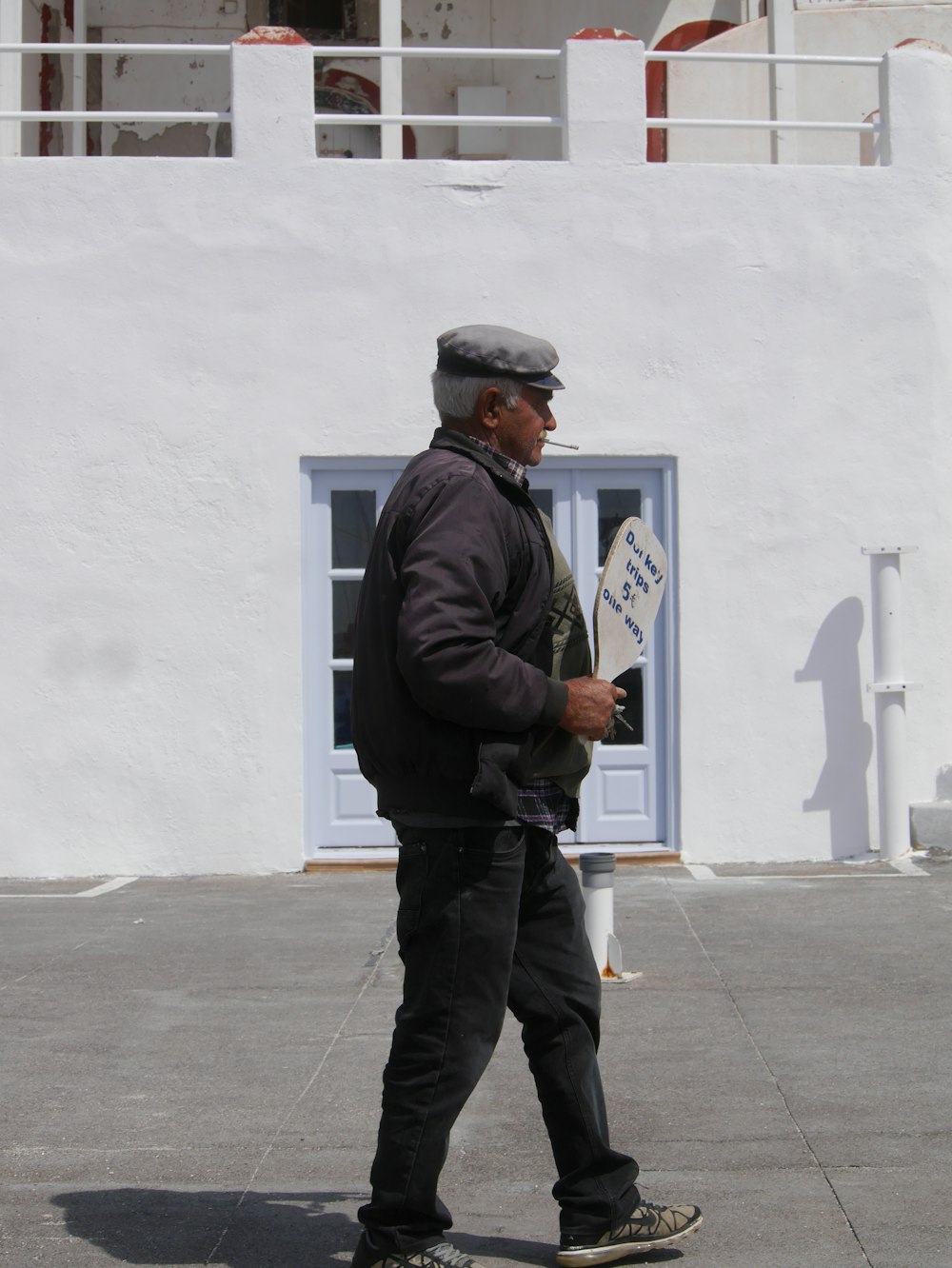 白いコンクリートの建物の近くで茶色の看板を掲げて歩く男