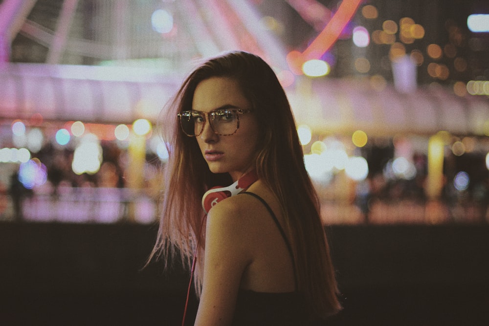 a woman wearing glasses standing in front of a ferris wheel