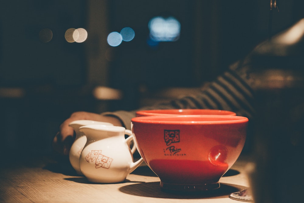selective focus photography of two red ceramic bowls near two white ceramic pitchers