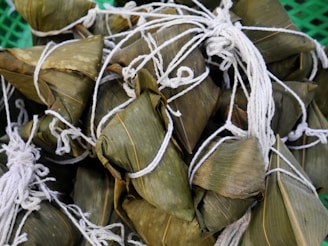 Bundles of food wrapped in green leaves and tied with white strings. The leaves have a natural texture with visible veins, and the strings are neatly tied, securing the packages.