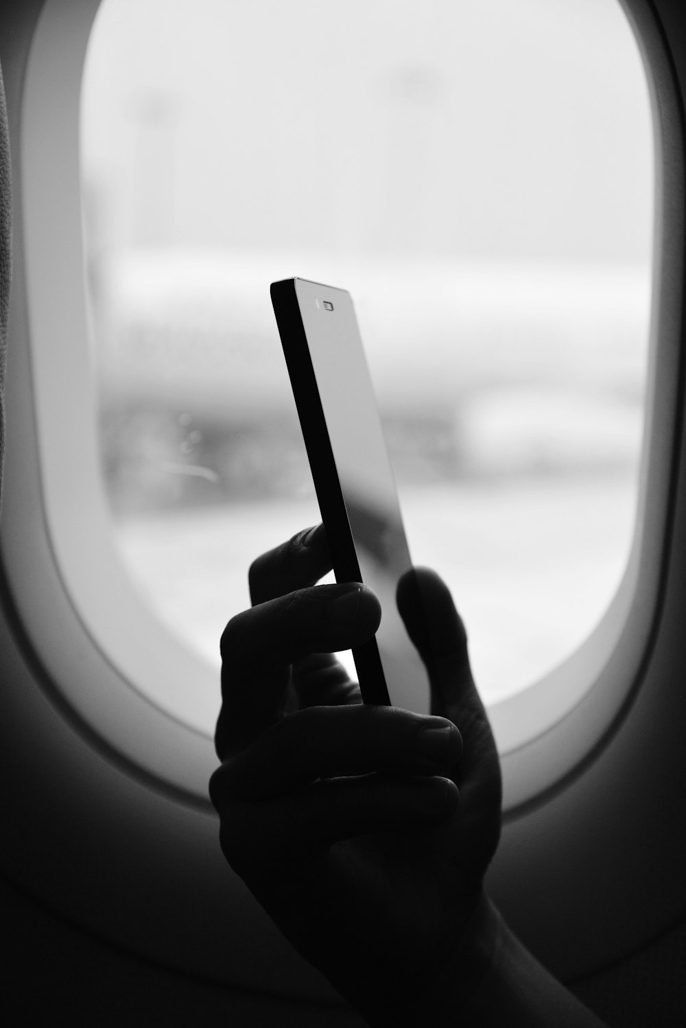 Graustufenfotografie einer Person, die ihr Smartphone neben dem Fenster hält