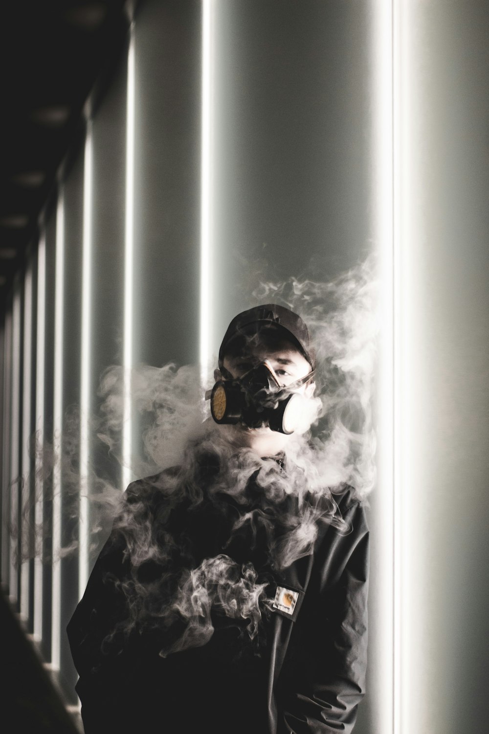 man wearing gas mask leaning on white concrete wall surrounded by smoke