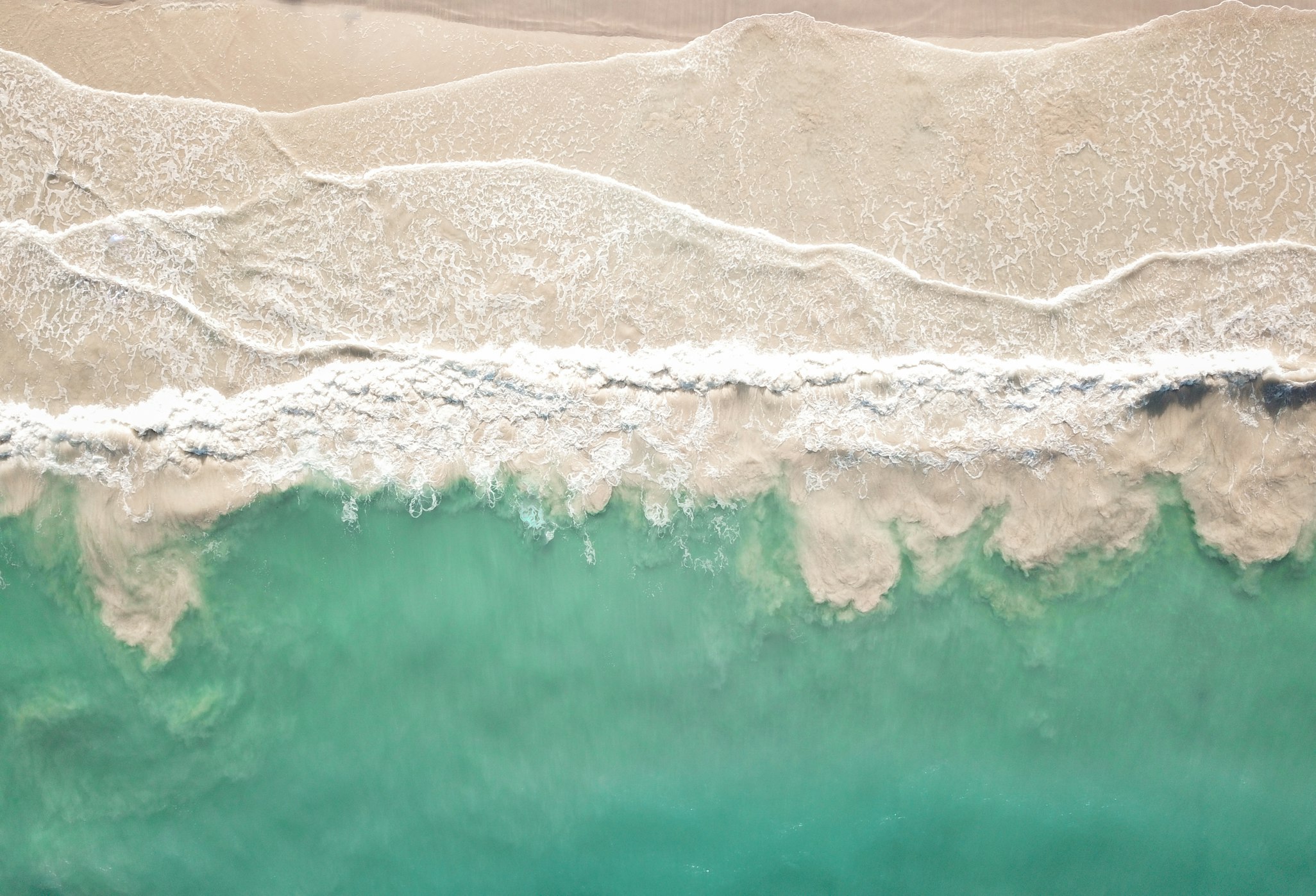 A sandy beach with teal colored water from above.