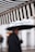 A striped awning appears prominently in the foreground, consisting of alternating black and white stripes. In the background, a person holds an umbrella, with the figure blurred and out of focus, suggesting a rainy day atmosphere.