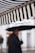 A striped awning appears prominently in the foreground, consisting of alternating black and white stripes. In the background, a person holds an umbrella, with the figure blurred and out of focus, suggesting a rainy day atmosphere.