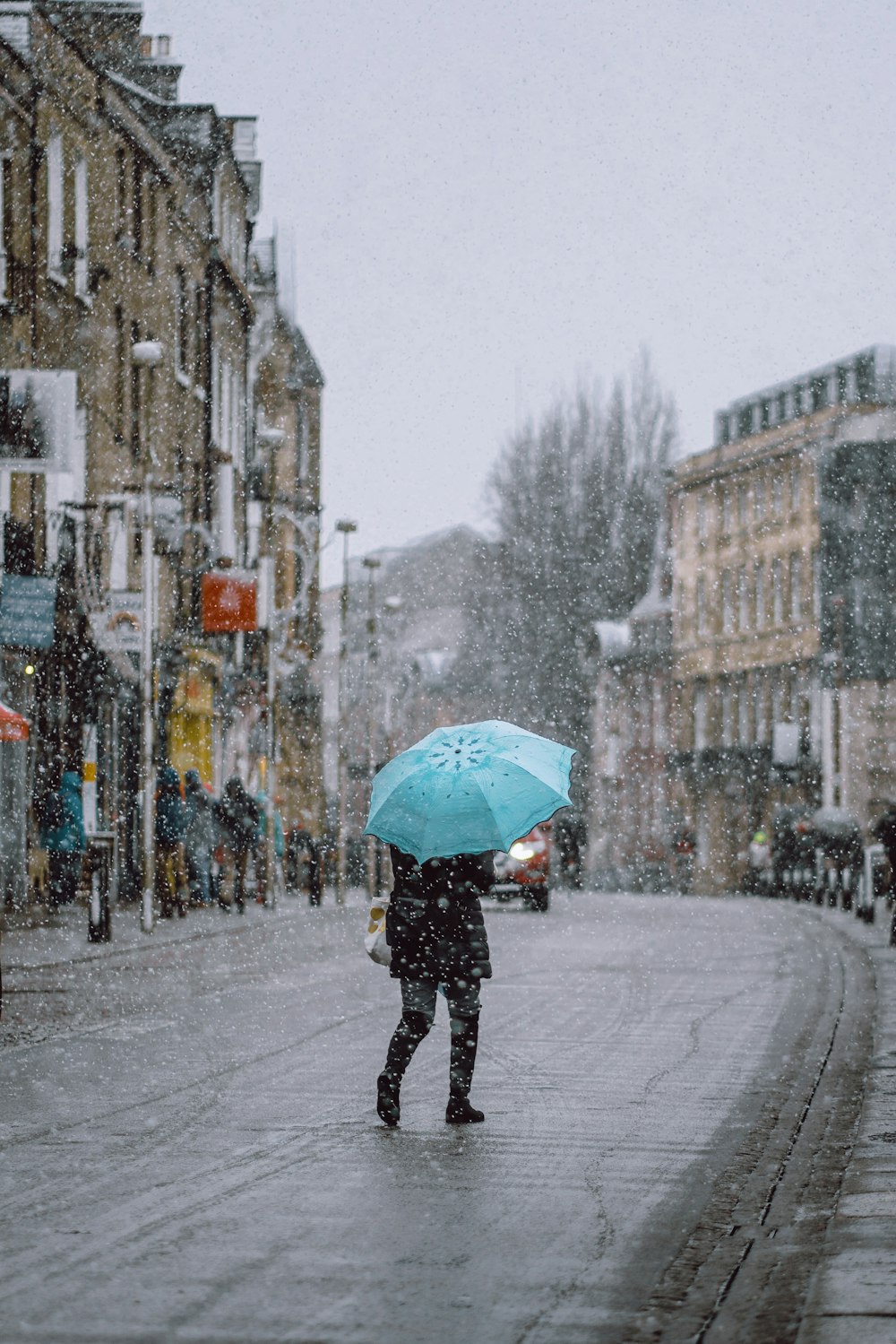 person using blue umbrella walking on street with falling snow
