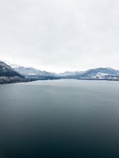 An expansive drone panorama of a serene lake reflecting the snow-capped Rockies under a bright sky.