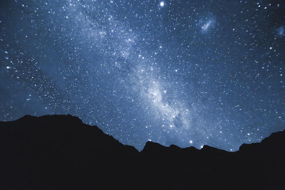 the night sky is filled with stars and the silhouettes of mountains