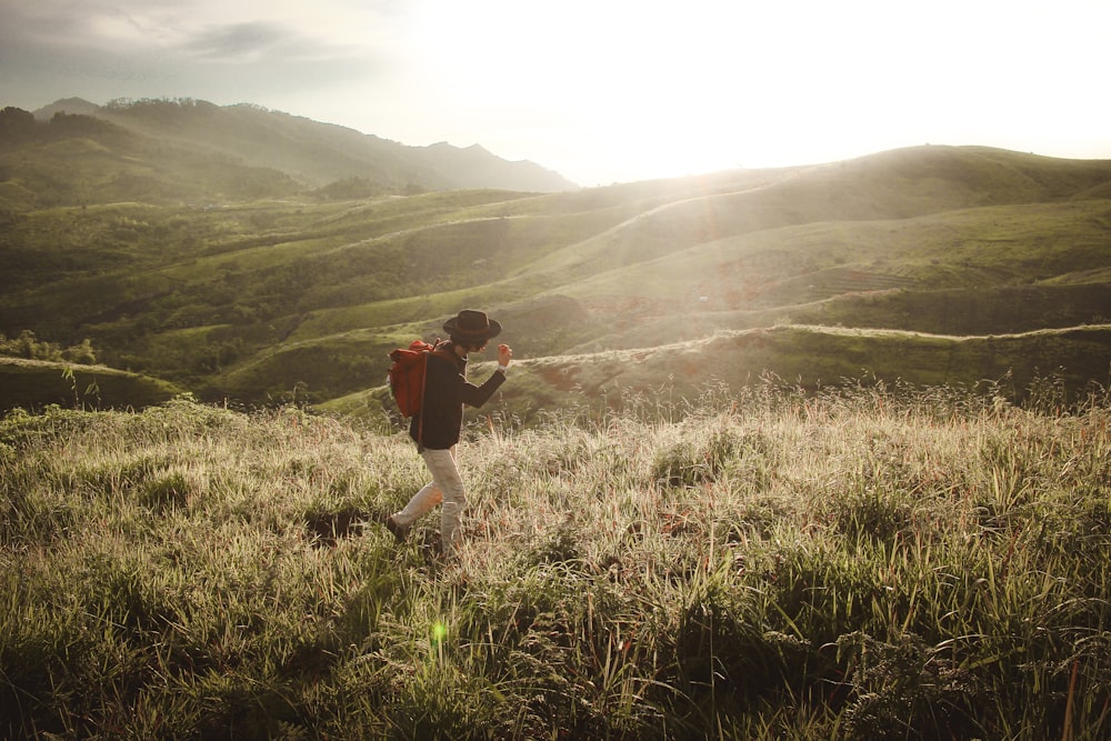 person walking in the middle of mountain grass field