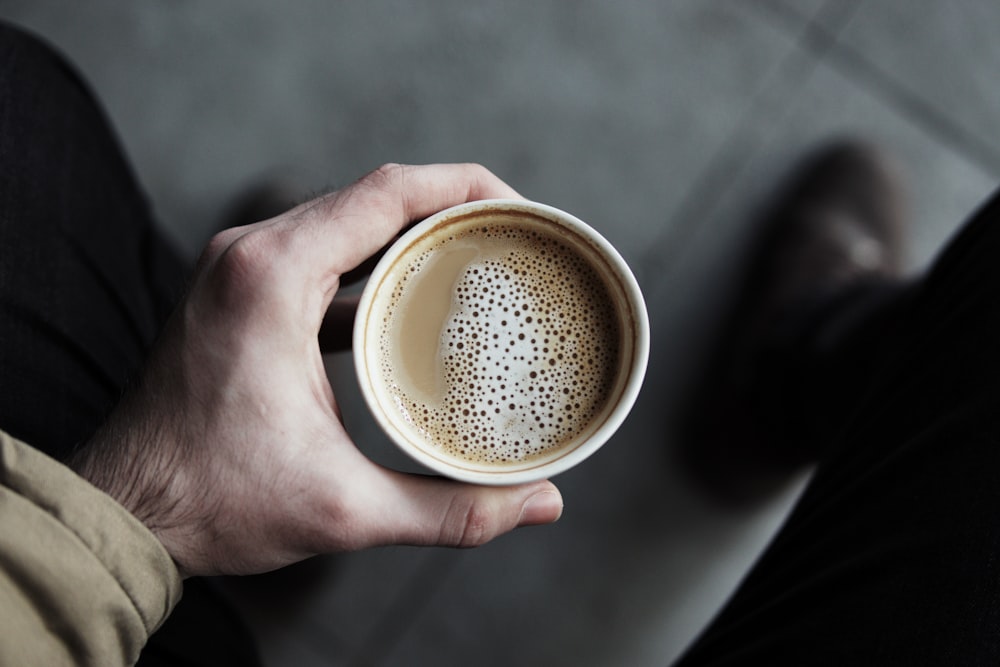 persona sosteniendo un vaso de papel blanco lleno de café