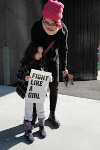 girl holding fight like a girl-printed paper beside woman holding plastic pack