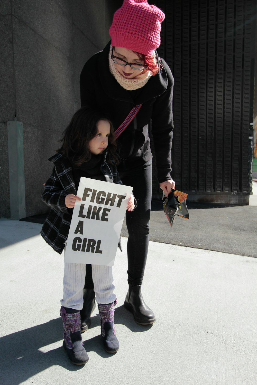 girl holding fight like a girl-printed paper beside woman holding plastic pack