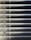 Horizontal blinds partially closed with minimal light seeping through, creating a pattern of alternating light and shadow. A pull cord hangs on the left side of the blinds.