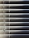 Horizontal blinds partially closed with minimal light seeping through, creating a pattern of alternating light and shadow. A pull cord hangs on the left side of the blinds.