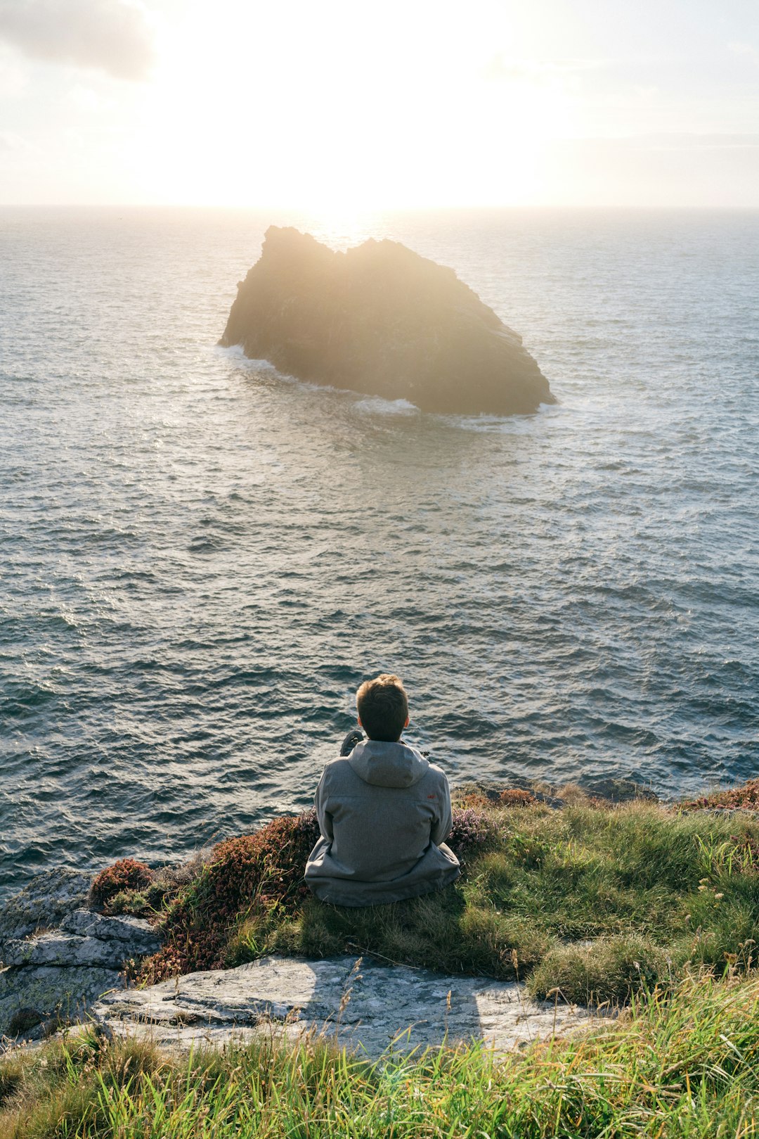 man sitting on grass beside ocean during daytime