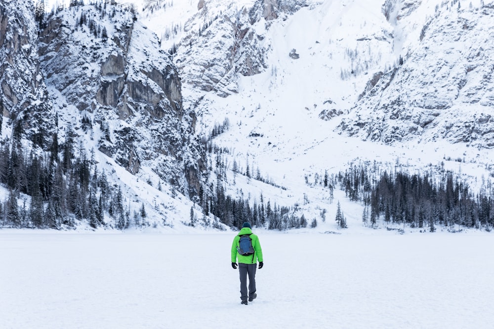 person in green jacket walking toward snow covered mountain