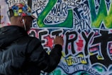 man spraying graffiti on wall during daytime