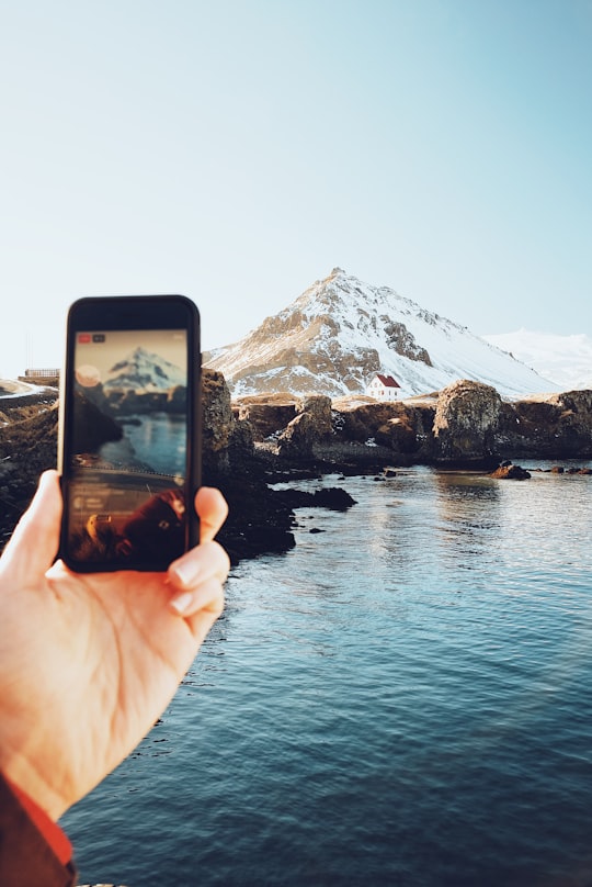 person taking picture on mountain covered with snow in Arnarstapi Iceland