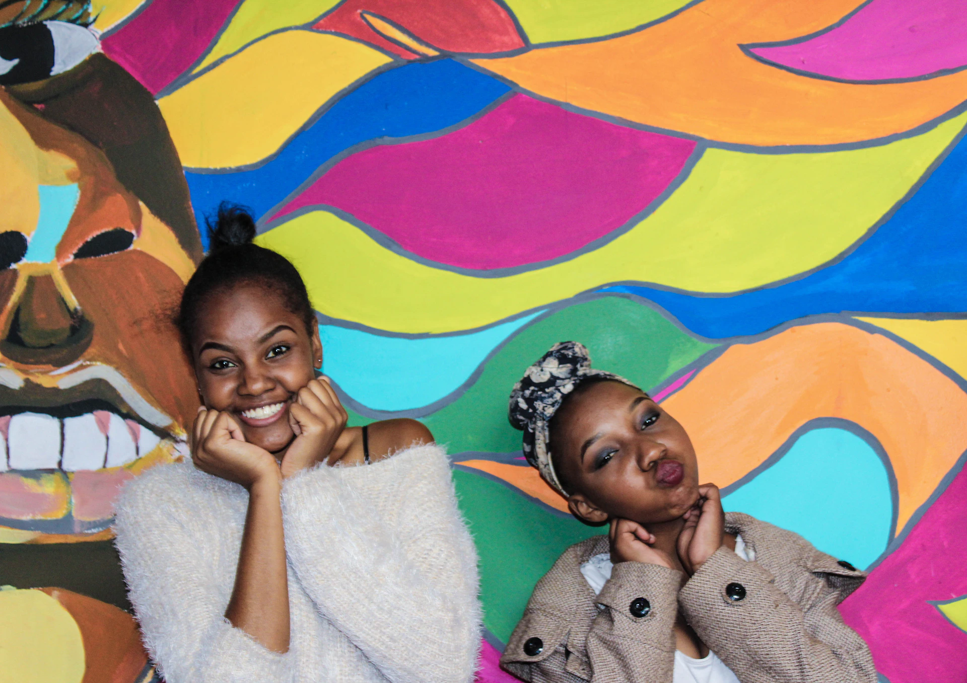 Two twins striking playful poses side-by-side in front of a bright, bold Twins Wiin event banner.