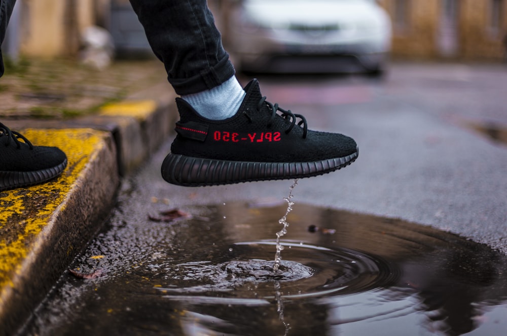 person wearing adidas Yeezy Boost 350 shoe above road puddle