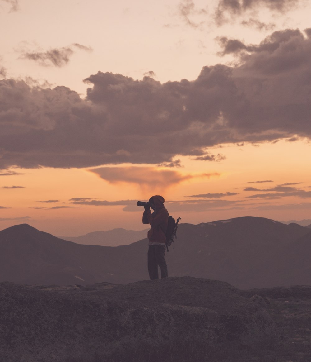 silhouette of man standing on top of mountain during sunset