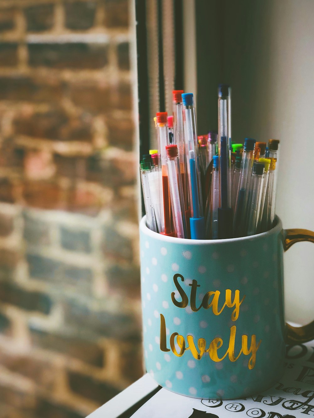 pens in blue ceramic mug in front of window during daytime