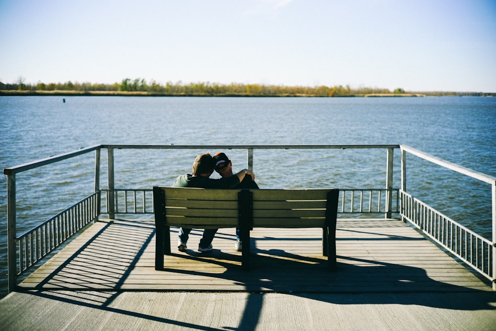 two person sitting on bench facing body of water