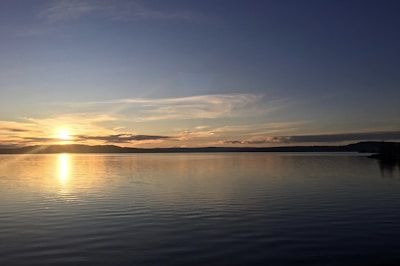 A serene lake reflecting the soft glow of a sunset behind distant hills.