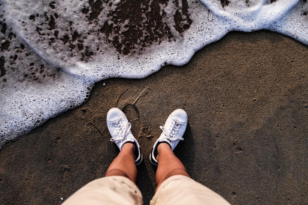 person wearing white shoes standing on sea shore