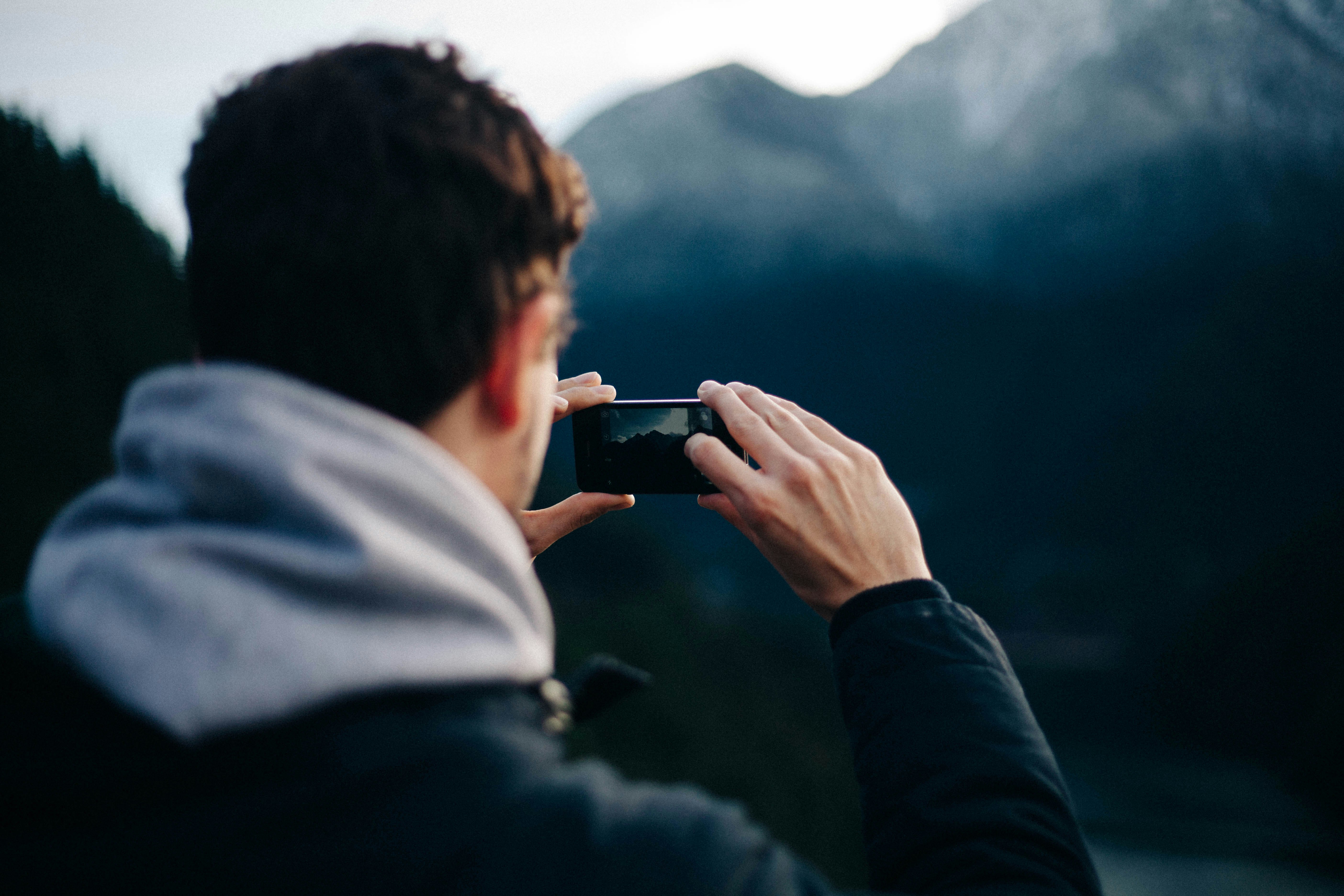 man holding smartphone taking photo of mountain